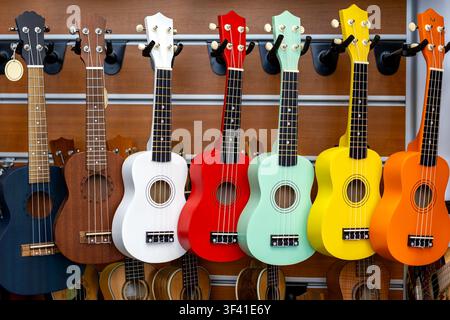 Colorful Ukuleles Displayed in a Music Shop. A colorful row of ukuleles hangs on a wooden music shop wall, featuring bright finishes, strings Stock Photo