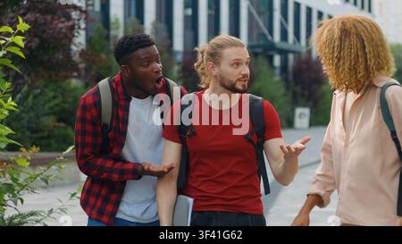 Group three multiethnic students talking emotional arguing smiling emotive discuss studying learning exams problem walking in city multiracial friends Stock Photo