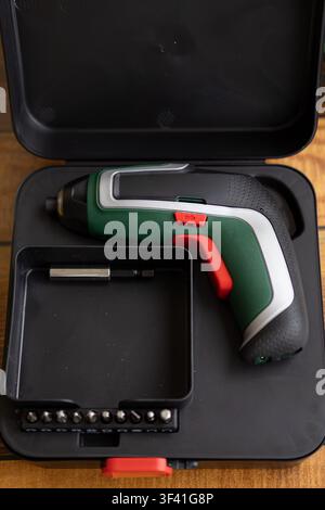 Cordless electric screwdriver rests inside an open storage case with interchangeable bits arranged beside it. Concept of tool organization, equipment Stock Photo
