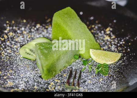Green sorbet made of blended cucumber, with fresh cucumber slices, a lime wedge, mint sprigs, and a dusting of powder or zest Stock Photo