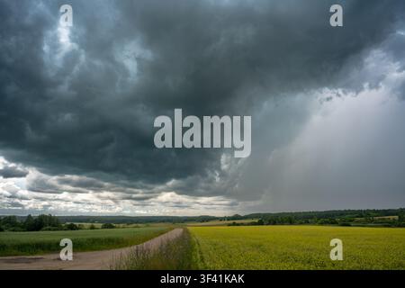 Massive dark thunderstorm clouds moving over a rural agricultural landscape with heavy rain in the distance. Dramatic weather scene Stock Photo