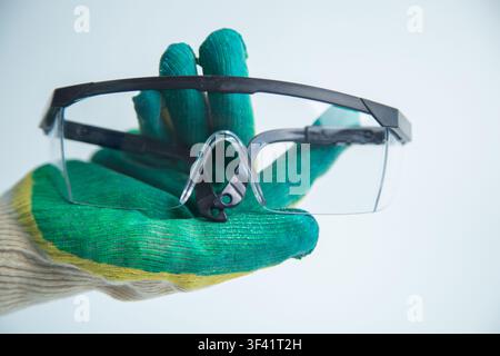 A hand in a protective glove holds transparent glasses with black frames right in front of the Stock Photo