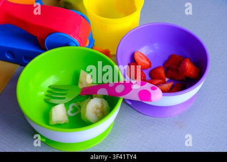 Brightly colored bowls hold sliced fruit. Fork and spoon rest beside the food. Childhood mealtime feels playful and cheerful. Ideal for nursery, paren Stock Photo