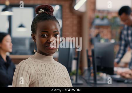 Focused portrait with smiling african american software developer looking at camera in artificial intelligence development agency around computer screens, showing developer teamwork, source code. Stock Photo