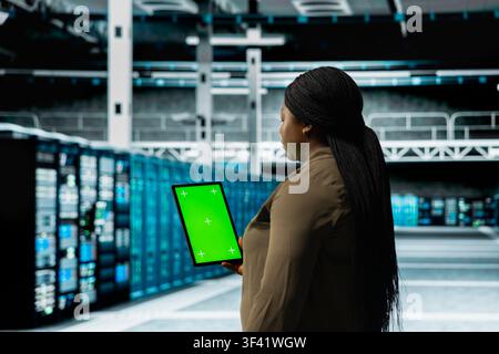 Admin using isolated screen digital device in data center to track metrics of gear used to host websites. Server hub worker upgrading rigs running companies databases using chroma key tablet Stock Photo