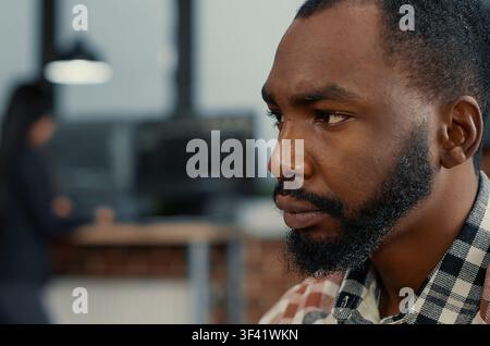 African American software developer types code while looking at a computer screen, with colleagues programming in the background in a software agency workflow. Stock Photo