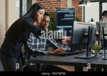 Two programmers carry a laptop with a coding interface toward a desk, preparing to discuss cloud computing and algorithm work with teammates. Stock Photo
