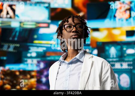 Doctor in lab coat monitoring interactive dashboards with medical research data and 3D anatomy models. Professional clinician standing near multimedia wall showing futuristic medical visual reports. Stock Photo