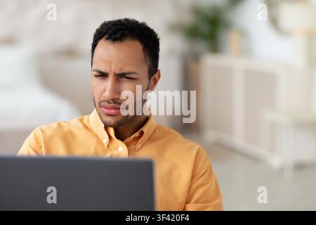 Focused Young Man Working On Laptop In Home Office, Looking Concerned, Business Concept Stock Photo