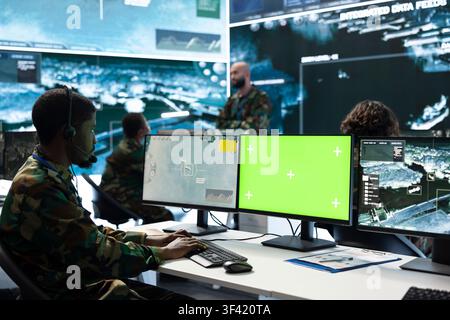 Mockup PC monitor used by army operator wearing communications headset. Military dispatcher coordinates radio updates using green screen chroma key computer Stock Photo