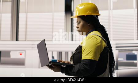 Specialist using laptop to conduct routine inspections in industry 4.0 plant producing renewable energy. Technician in photovoltaics smart factory testing equipment using notebook, camera B Stock Photo