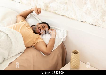 Happy Hispanic Man Stretching In Bed After Waking Up, Morning Routine Concept Stock Photo
