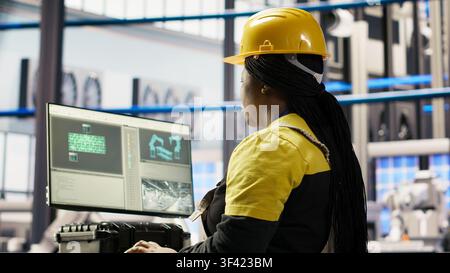 Smart solar panels factory worker typing on PC keyboard, testing automated systems, doing maintenance. Woman in industry 4.0 photovoltaics plant using computer to inspect gear and fix bugs, camera B Stock Photo