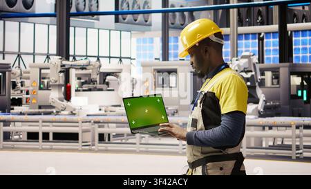 Solar panels factory engineer analyzes performance data with green screen laptop to predict gear failures. Photovoltaics plant worker uses mockup notebook to follow maintenance procedures, camera A Stock Photo