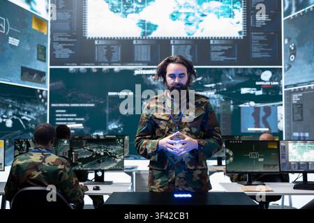 Army officer uses hand gestures to control holographic battlefield projection in command center. Military personnel analyzing tactical data while monitoring target movement Stock Photo