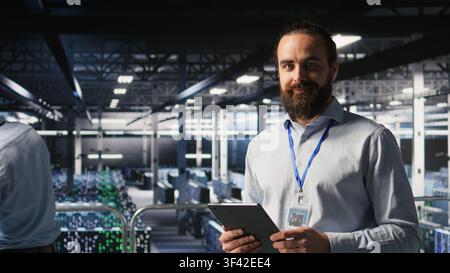 Portrait of smiling engineer in data center monitoring neural network LLM visualization. Cheerful server hub IT specialists overseeing rigs powering machine learning processes, Stock Photo