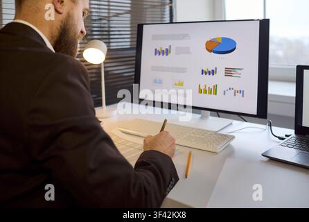 Businessman reviewing charts on desktop monitor, planning strategy at office desk Stock Photo