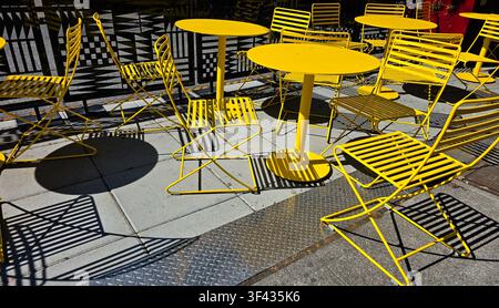 Modern Yellow Outdoor Cafe Tables and Chairs with Geometric Shadows on Urban Patio Stock Photo