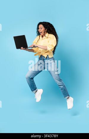 Excited Young Hispanic Woman Jumping While Using Laptop, Happy Business Concept Stock Photo