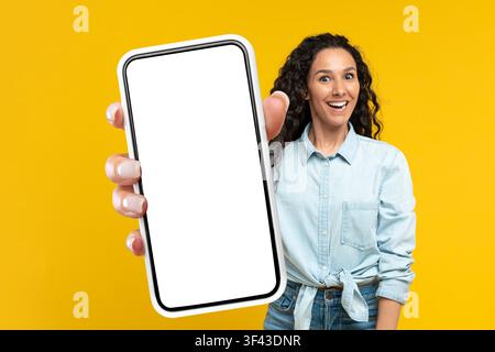 Smiling Hispanic Woman Holding Smartphone With Blank Screen, Yellow Background Stock Photo