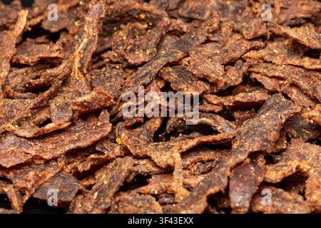 Macro photograph of a dense pile of homemade beef jerky strips coated in savory spices and red pepper flakes. High-resolution texture. Stock Photo