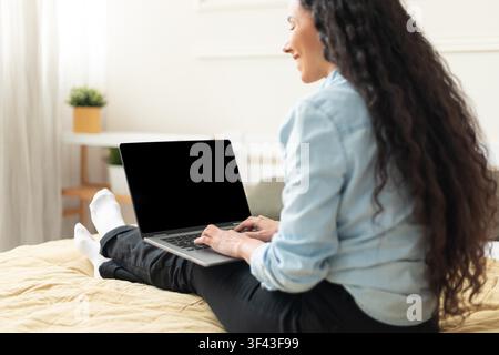 Smiling Young Woman Working On Laptop Sitting On Bed, Home Office Concept Stock Photo