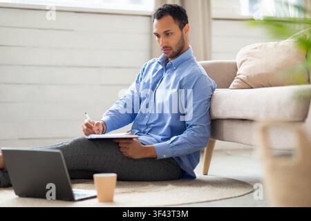 Focused Young Man Writing Notes, Working On Laptop At Home, Business Concept Stock Photo