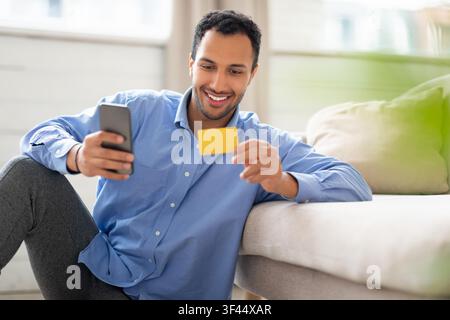 Smiling Young Hispanic Man Shopping Online With Credit Card At Home, Business Concept Stock Photo
