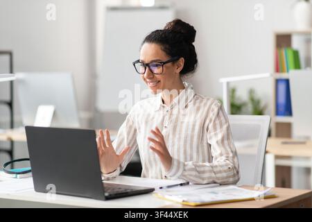 Smiling Young Mixed Race Woman Engaging In Video Call At Home Office, Business Concept Stock Photo