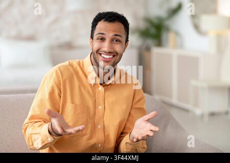Smiling Young African American Man Gesturing In Living Room, Business Concept Stock Photo