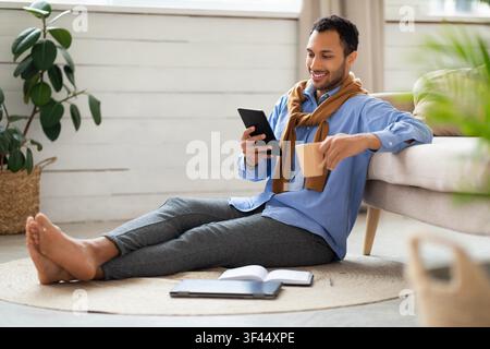 Smiling Young Male Using Tablet With Coffee Cup At Home, Relaxing Lifestyle Concept Stock Photo