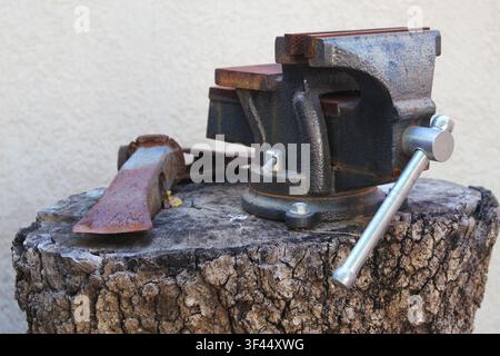 Rusty bench vice (bench vise) over a oak trunk. Concept: blacksmith, smith, prensa mecanica, tornillo de banco, taller de torno,lathe workshop Stock Photo