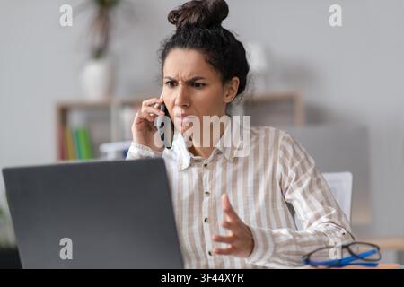 Worried Hispanic Female Entrepreneur Talking On Phone In Office, Business Concept Stock Photo