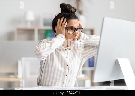 Worried Hispanic Female Office Worker Experiencing Stress While Working On Computer At Desk Stock Photo