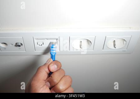 Connecting a blue ethernet cable to a wall socket Stock Photo