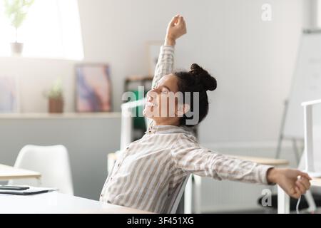 Smiling Young Woman Stretching In Office, Happy And Relaxed, Wellness Concept Stock Photo