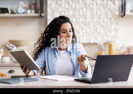 Focused Latina Woman Studying Online And Taking Notes In Home Office, Business Concept Stock Photo