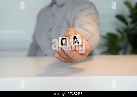 Close-up of a hand holding QA wooden blocks, representing quality assurance, inspection, testing, compliance, process control, auditing, and business Stock Photo