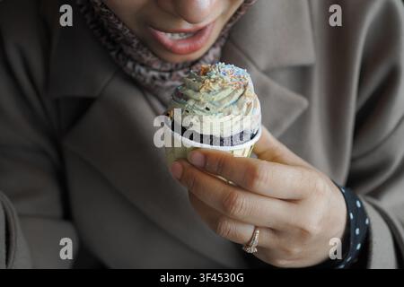 A woman is holding a cupcake with colorful frosting and sprinkles. Stock Photo
