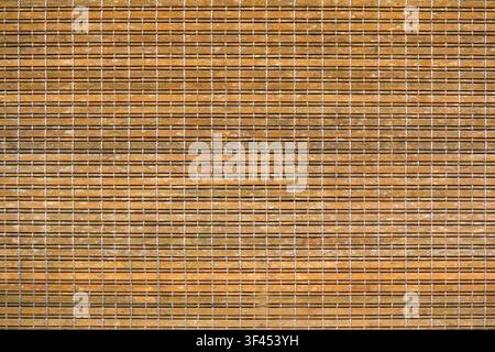 Close-up of a natural bamboo mat or blind, featuring horizontal light brown wooden slats intricately woven together with contrasting white threads. A Stock Photo