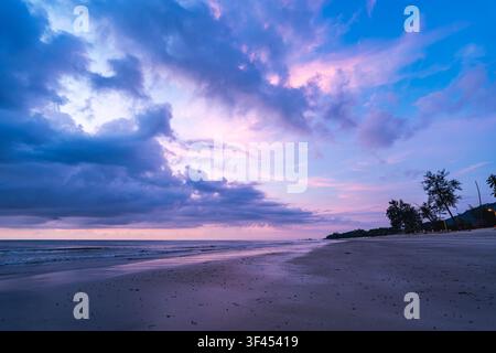 Serene view of a pristine tropical beach at sunrise. A breathtaking sky, painted with vibrant purple, pink, and blue clouds, reflects beautifully on t Stock Photo