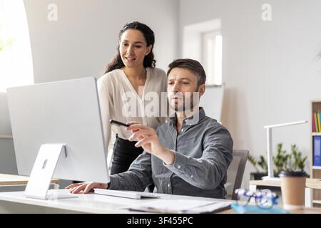 Woman Standing Behind Man Working On Computer, Office Environment, Business Concept Stock Photo