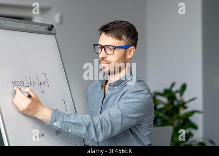 Man Writing On Whiteboard In Office, Focused Young Professional, Business Concept Stock Photo