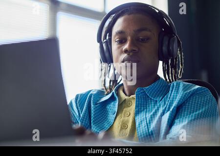 Black Man Wearing Headphones Working on Laptop for Remote Job Stock Photo