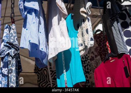 Close up shot of colorful shirts and blouses hanging on display at an outdoor market Stock Photo