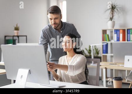 Smiling Hispanic Woman And Man Working Together At Computer In Modern Office, Business Concept Stock Photo
