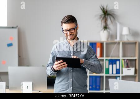 Smiling Young Man Using Tablet In Modern Office, Business Concept Stock Photo