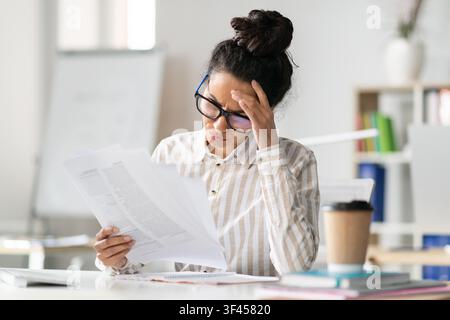 Worried Young Black Woman Reviewing Documents In Office, Business Concept Stock Photo