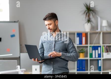 Focused Caucasian Man Using Laptop In Modern Office, Business Concept Stock Photo