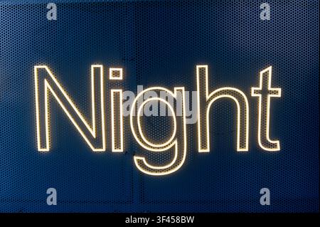 Night word illuminating a dark perforated metal background, signifying evening or leisure Stock Photo